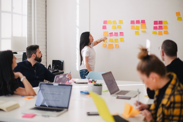 Frau moderiert ein Team-Meeting stehend vor einer Wand mit angeklebten bunten Klebezetteln