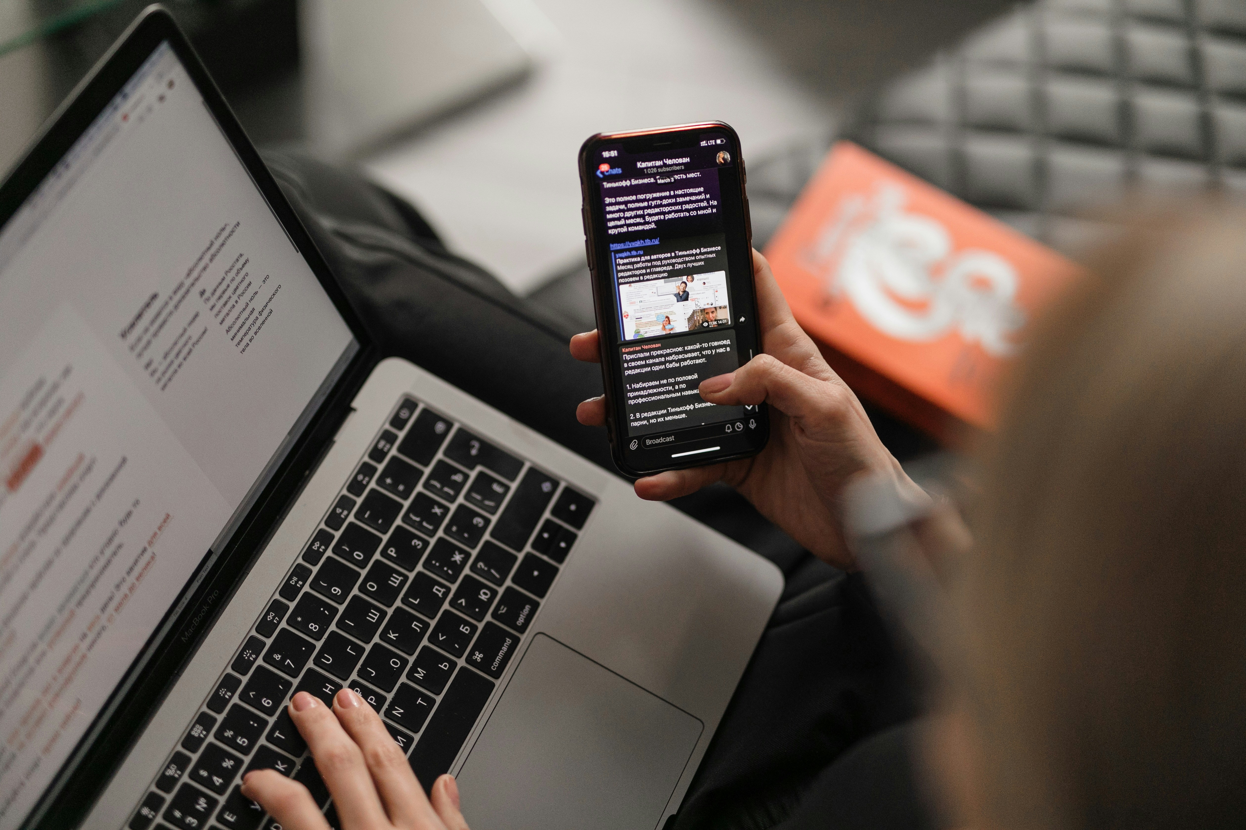Person die am Notebook-PC arbeitet und dabei Nachrichten auf dem Smartphone liest